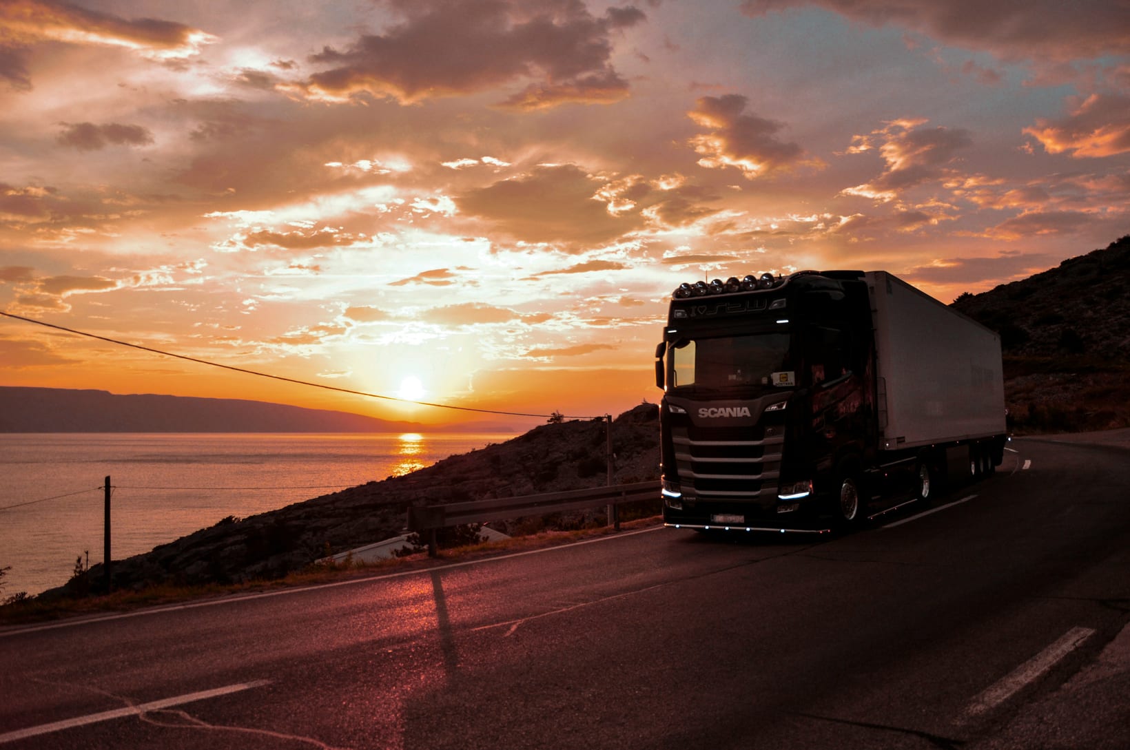 A lorry on a coastal road at sunset.